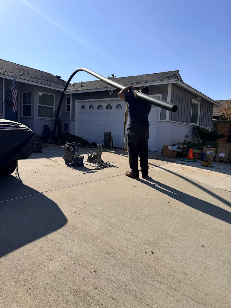 GR Plumbing technician carrying a trenchless sewer pipe-bursting line across a residential driveway