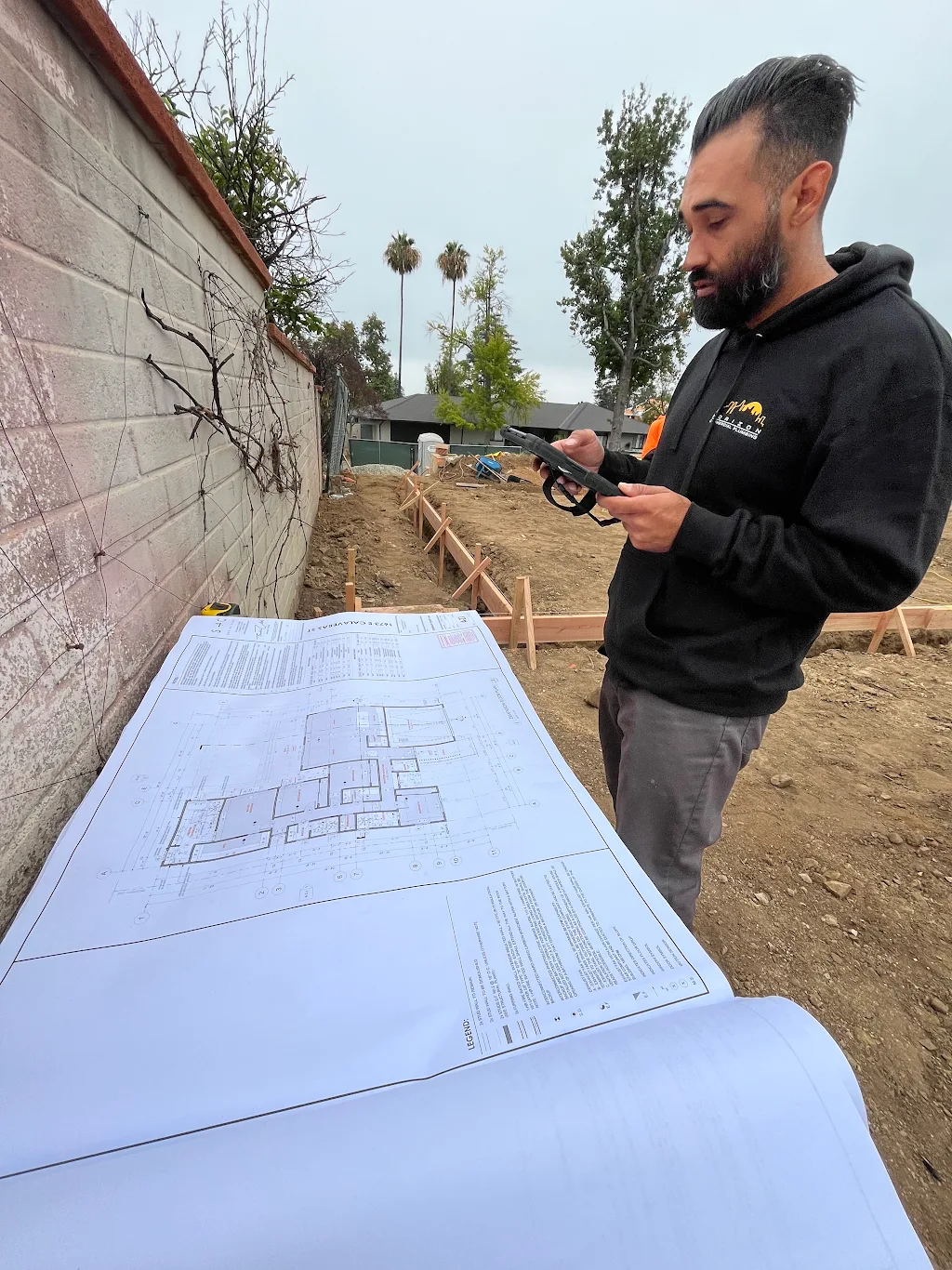 A Horizon Commercial Plumbing project lead reviewing blueprints over an excavated foundation trench in Altadena