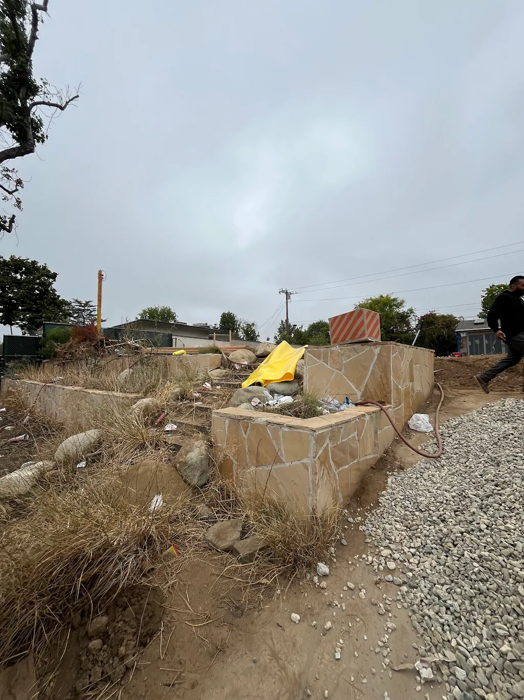 A surviving stone retaining wall on a cleared Altadena lot, with new gravel pad and construction staging
